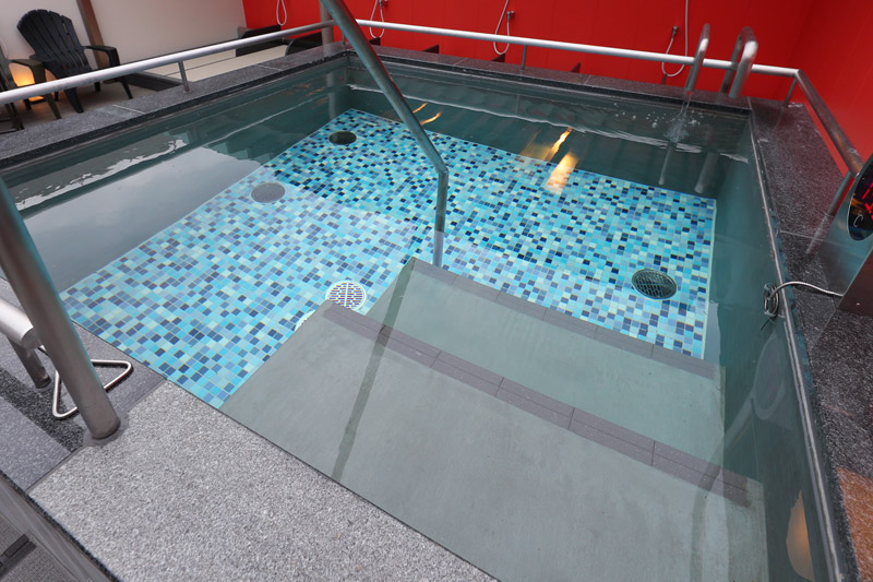 増設された冷水風呂の浴槽。中に2段の階段があり底には青色のモザイクタイルが敷き詰められている