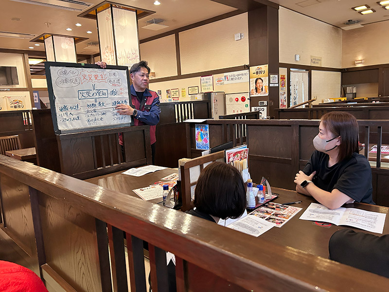 火災発生時の対応の手順が書かれたパネルを持って男性が説明している写真